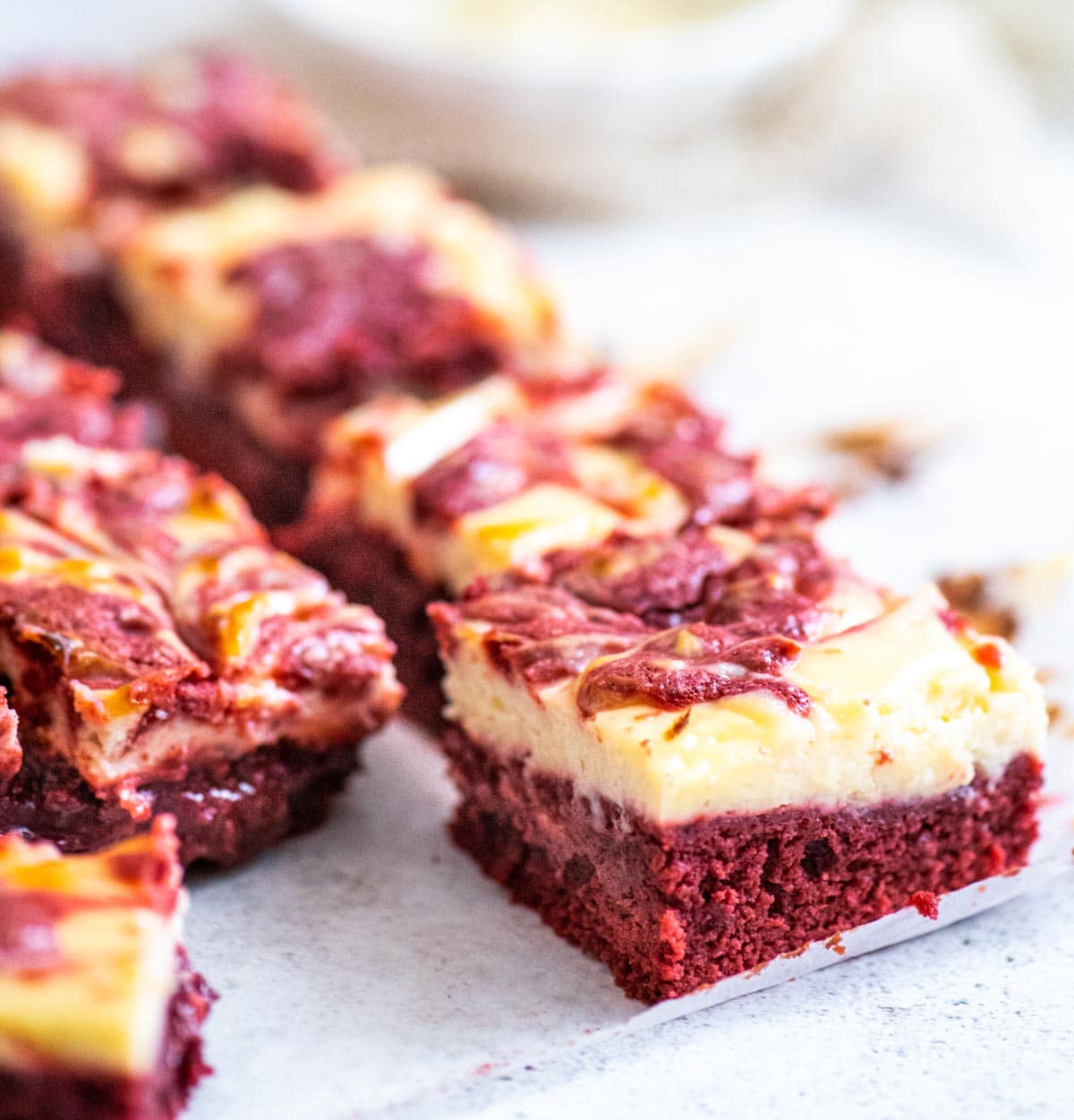 A single piece of red velvet brownie with cheesecak topping in the foreground  