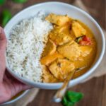 Hand holding a bowl of Thai chicken curry and rice
