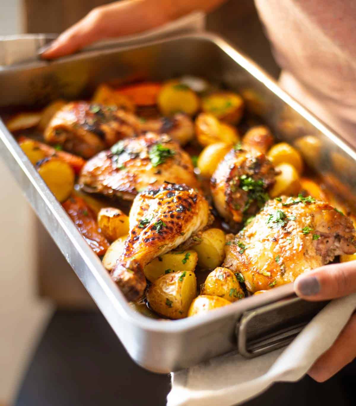 hands holding a tray with baked chicken and potatoes 