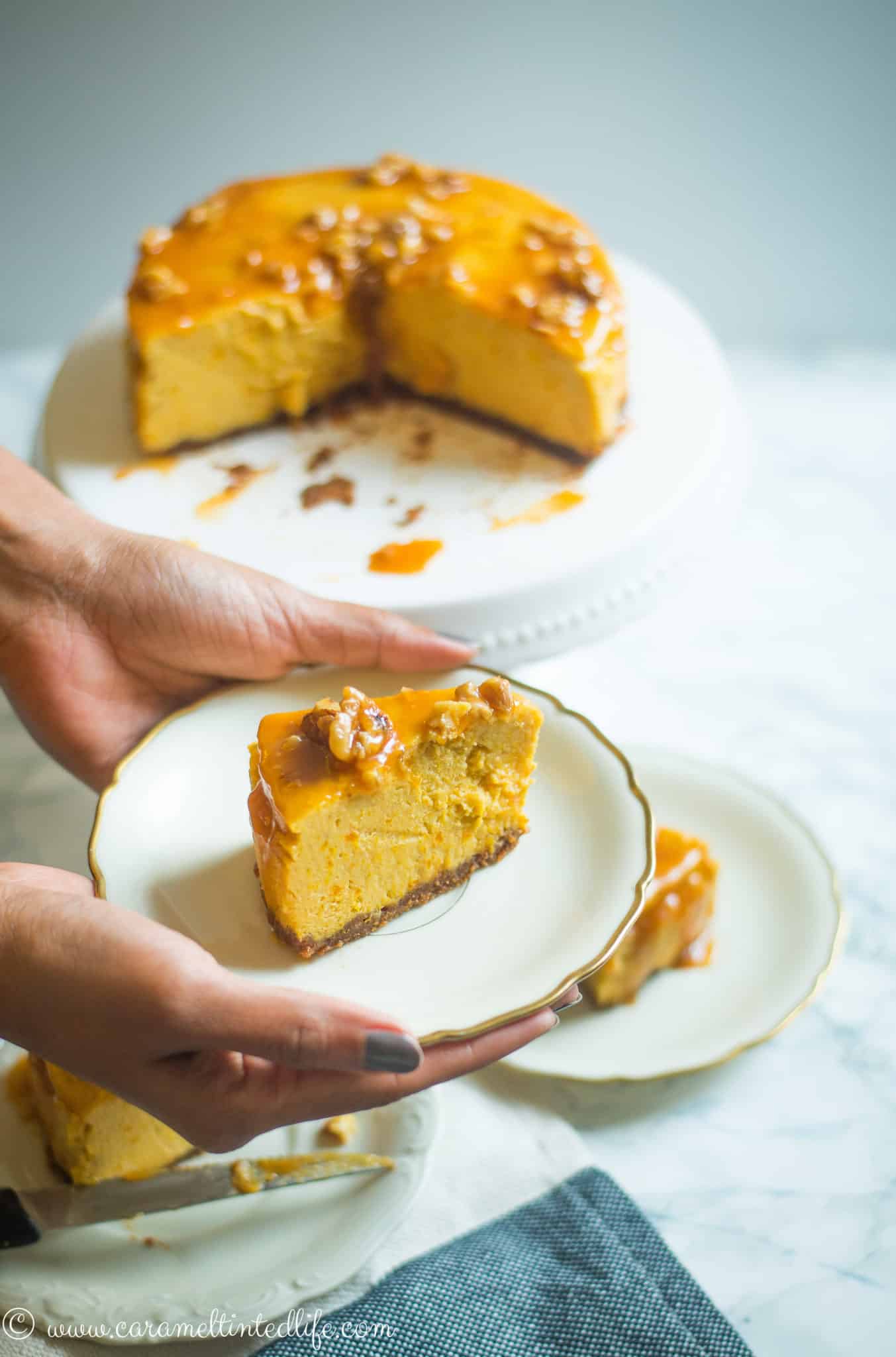 A single slice of Pumpkin Cheesecake on a plate, held by two hands