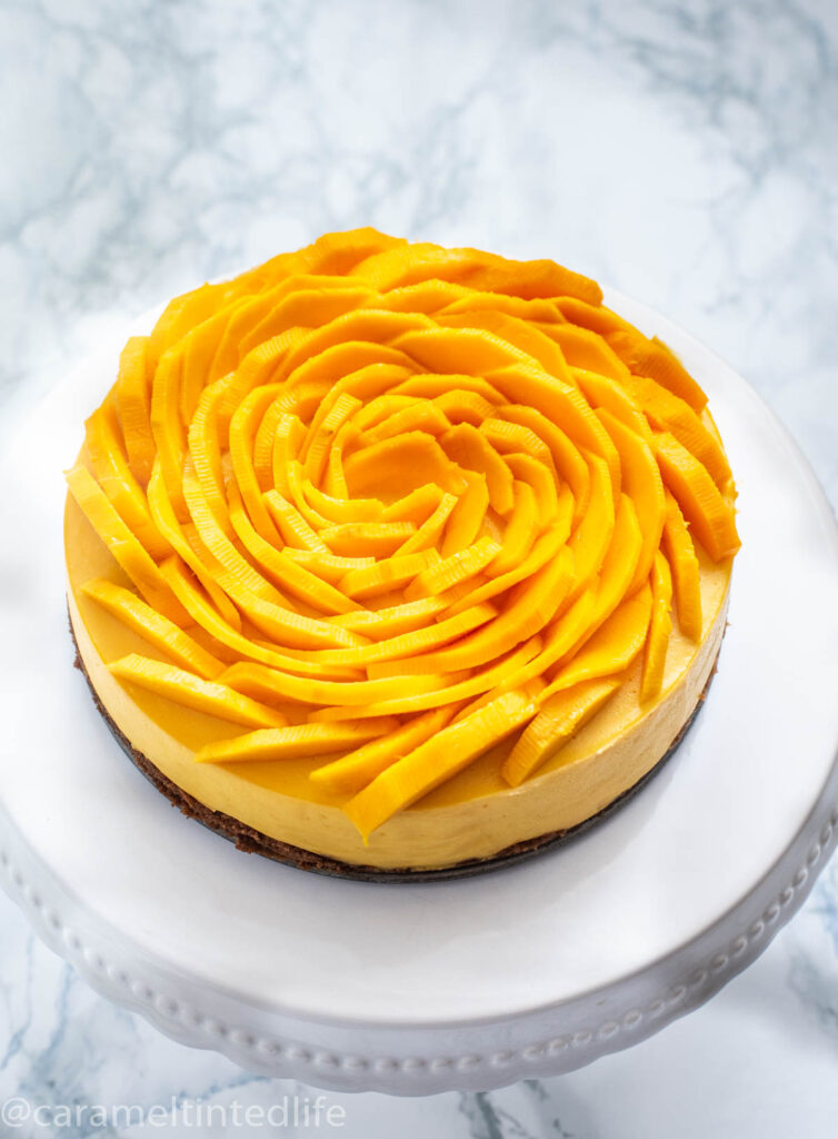 Mango cheesecake with mango slices on top on a cake stand