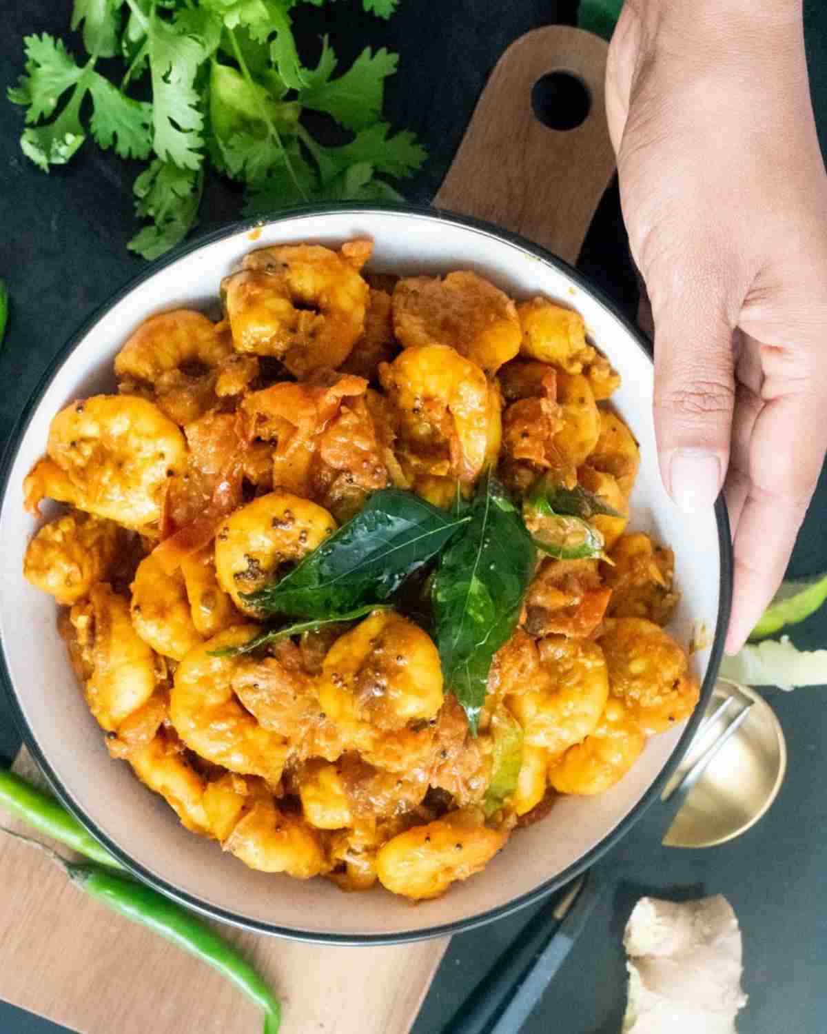 Hand holding a bowl of shrimp masala