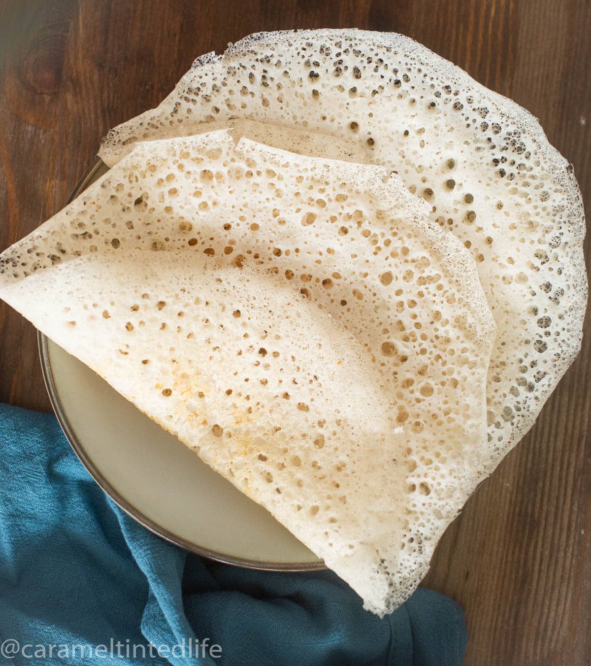 Two appams folden on a plate on a wooden board