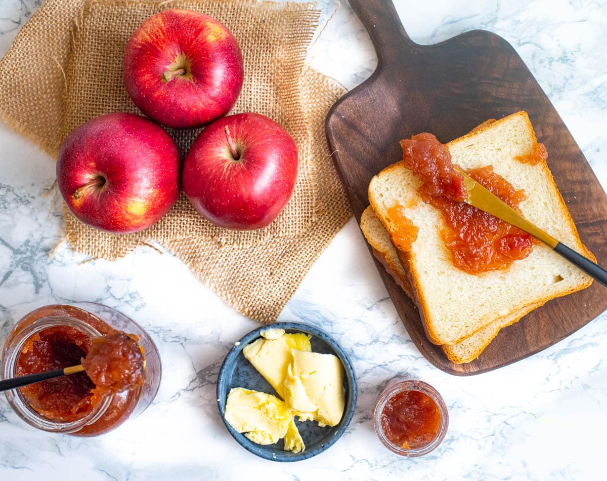 Sandwich bread with apple jam and knife, butter in a dish and apples