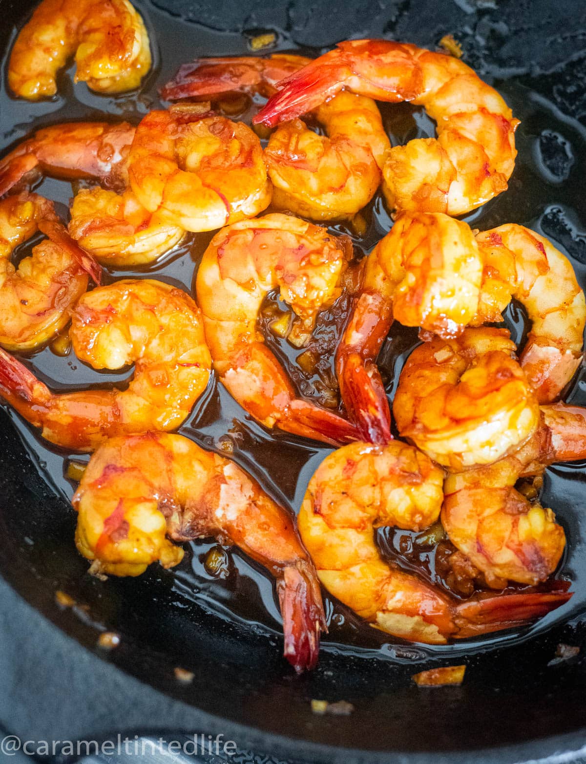 Prawns cooking in a honey garlic sauce in a cast iron skillet pan