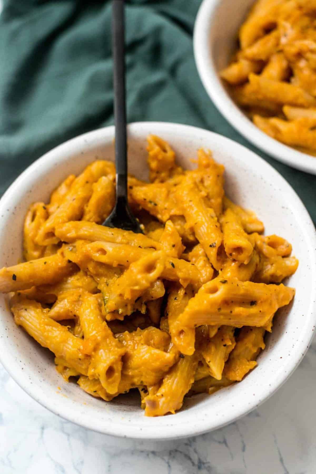 Pasta cooked in a butternut squash saucein a white bowl with a black fork