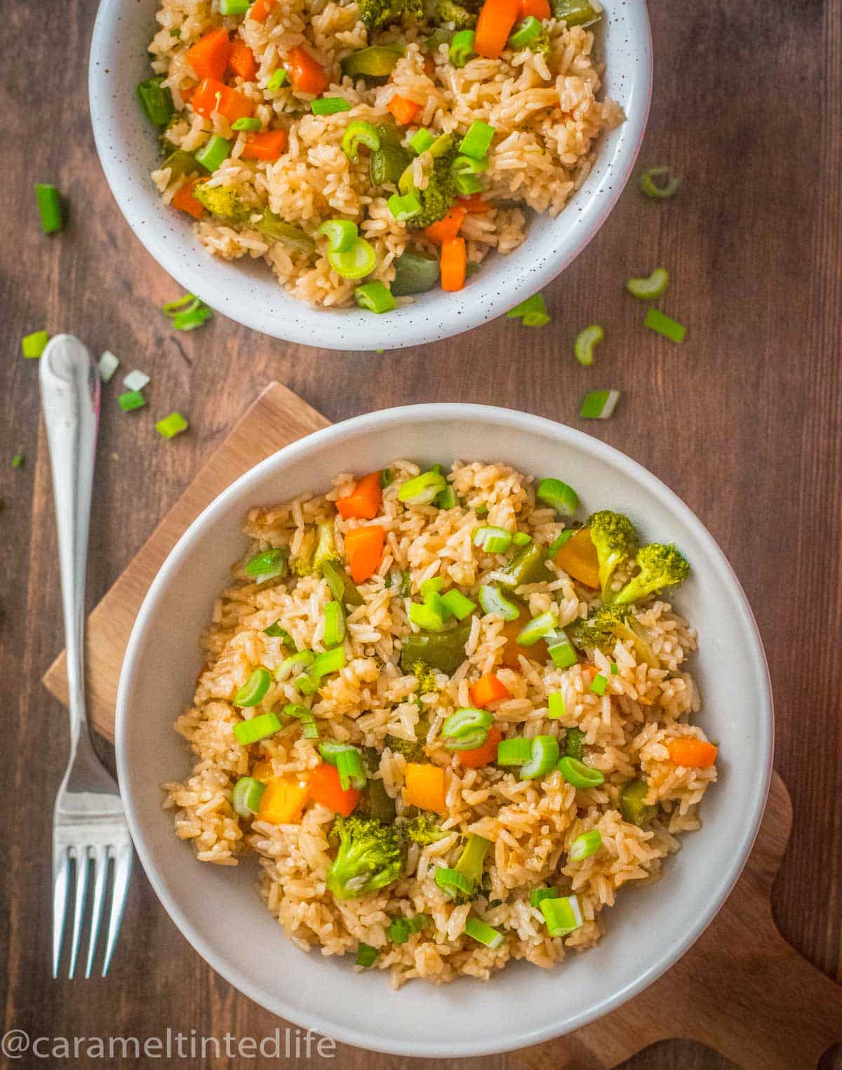 Two bowls of fried rice and a fork on a wooden backdrop