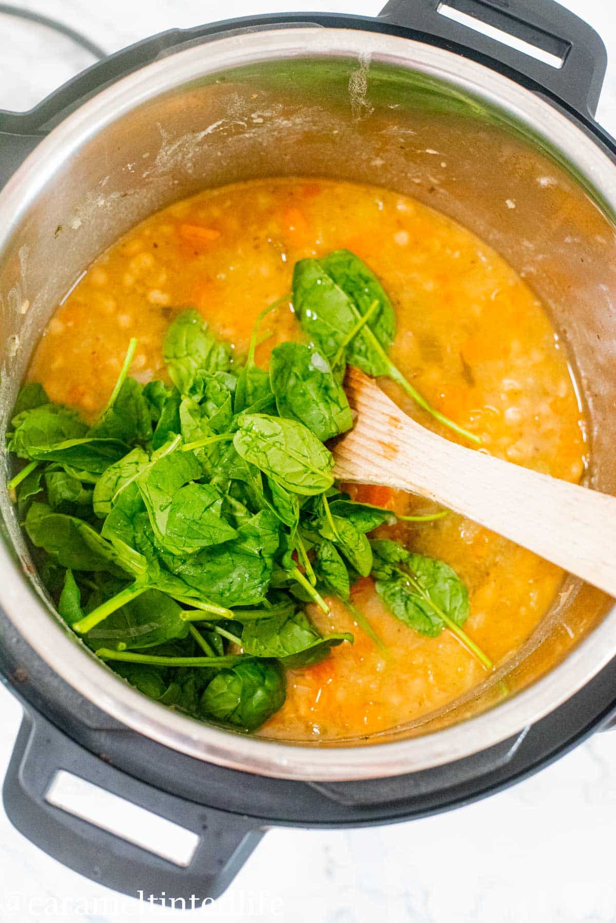 Spinach leaves being added to white bean soup in the Instant Pot