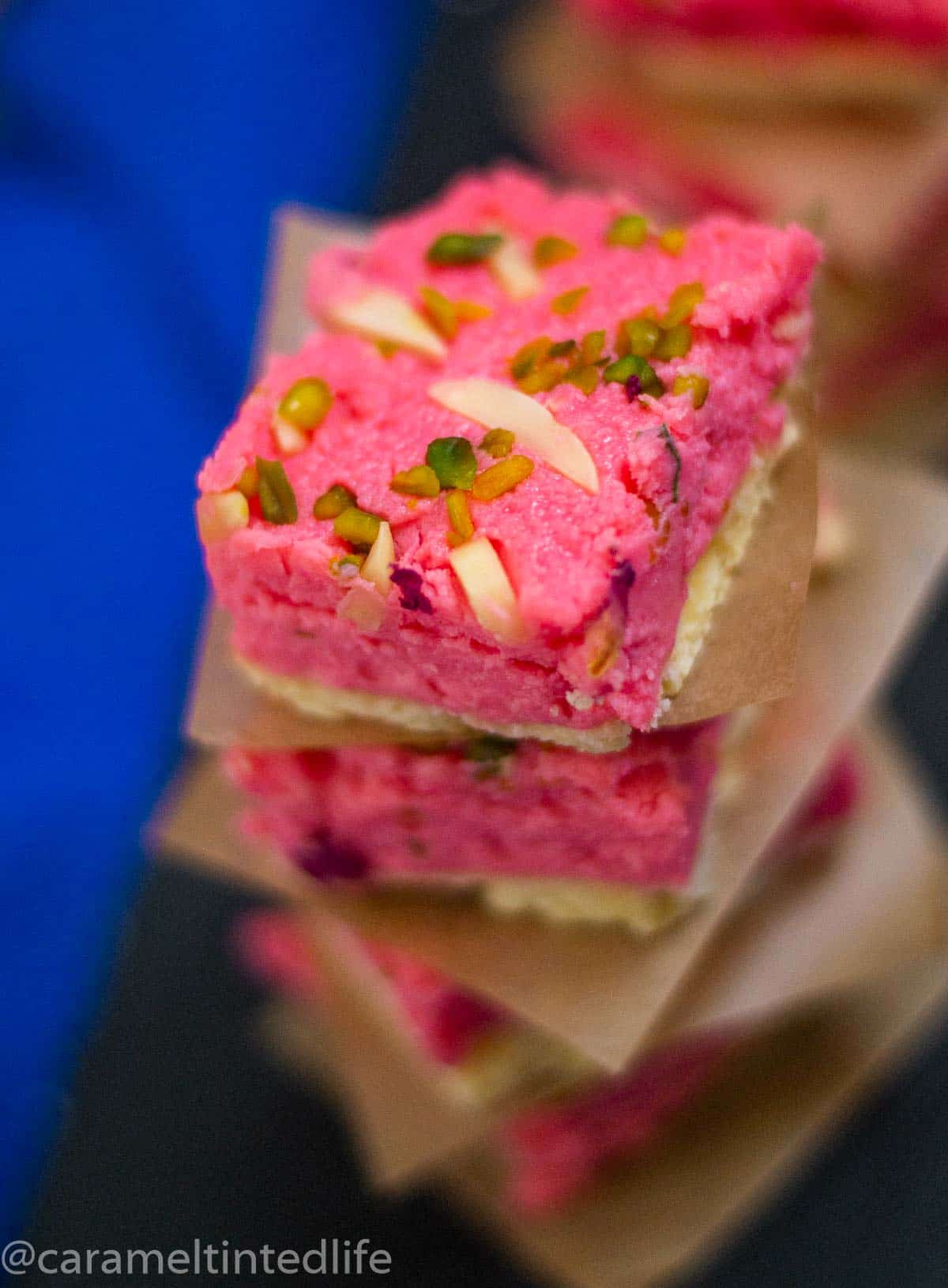 Close up of a piece of rose kalakand garnished with pistachios and almonds