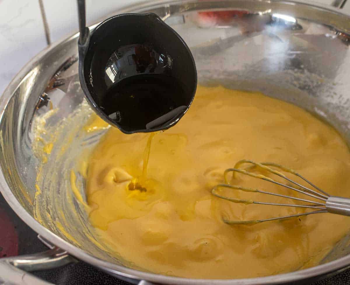 A ladle pouring hot oil and ghee into a wok with chickpea flour and sugar syrup