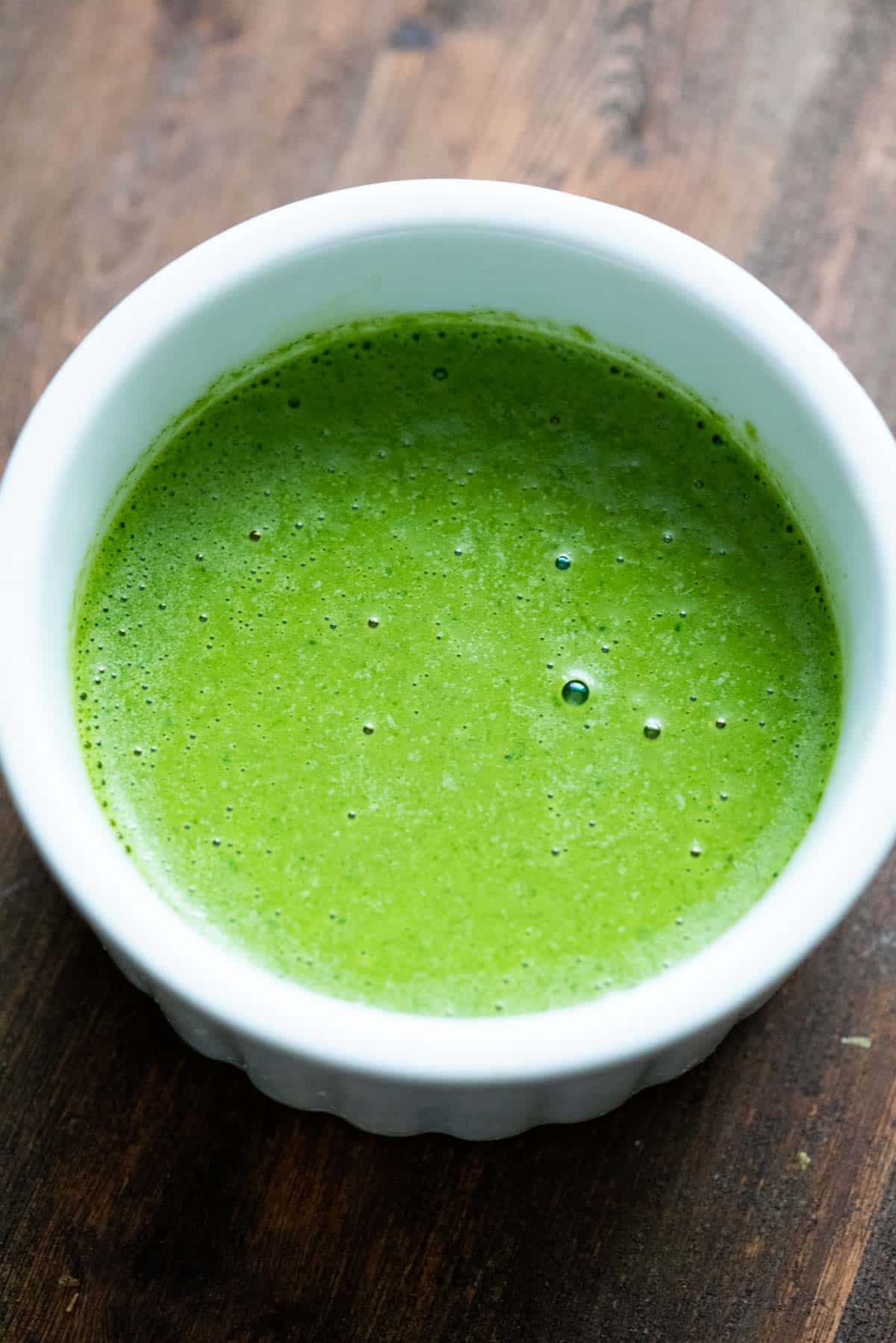 Thick green chutney with cashews blended in, ina white ramekin on a wooden backdrop