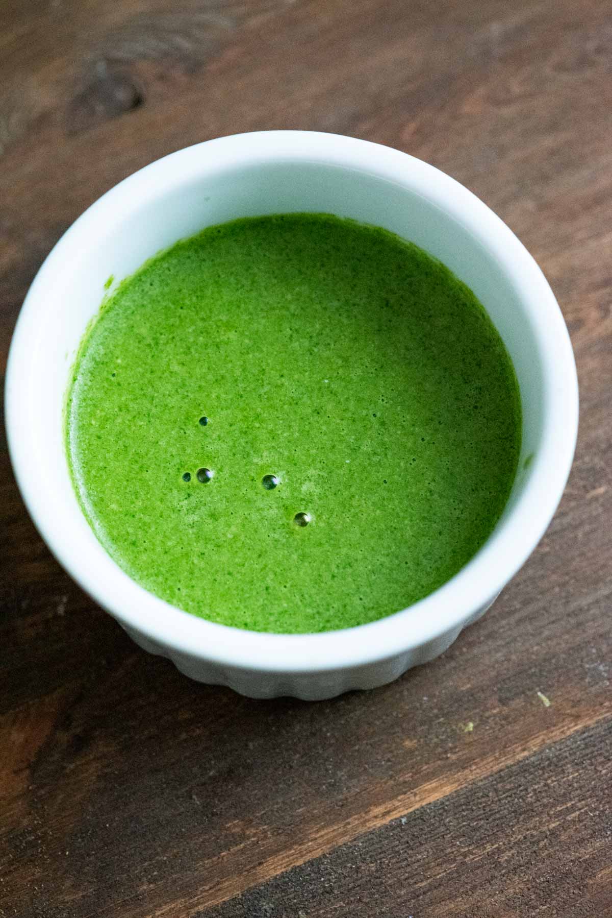 Green chutney with yogurt added to it, in a white ramein on a wooden backdrop