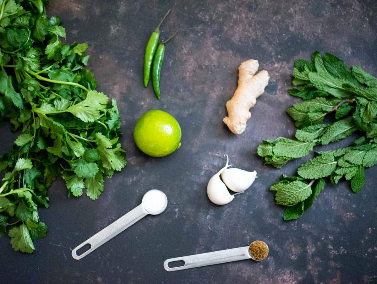 Ingredients required to make green chutney on a brown backdrop