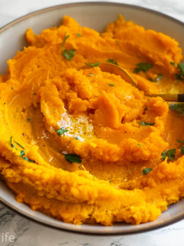 A bowl of mashed sweet potatoes with a spoon in them
