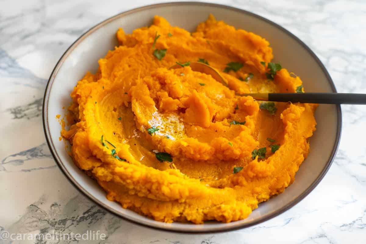 A bowl of mashed sweet potatoes with a spoon in it