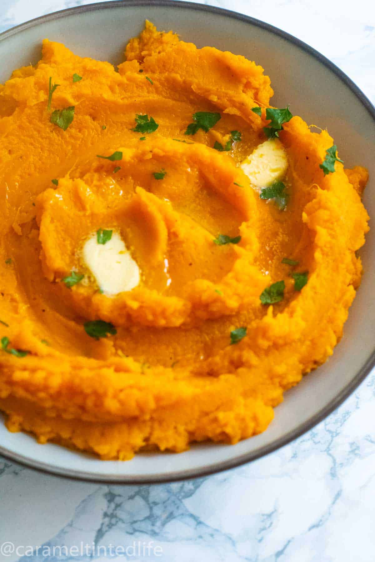 Mashed sweet potatoes in a bowl with melted butter and parsley garnish
