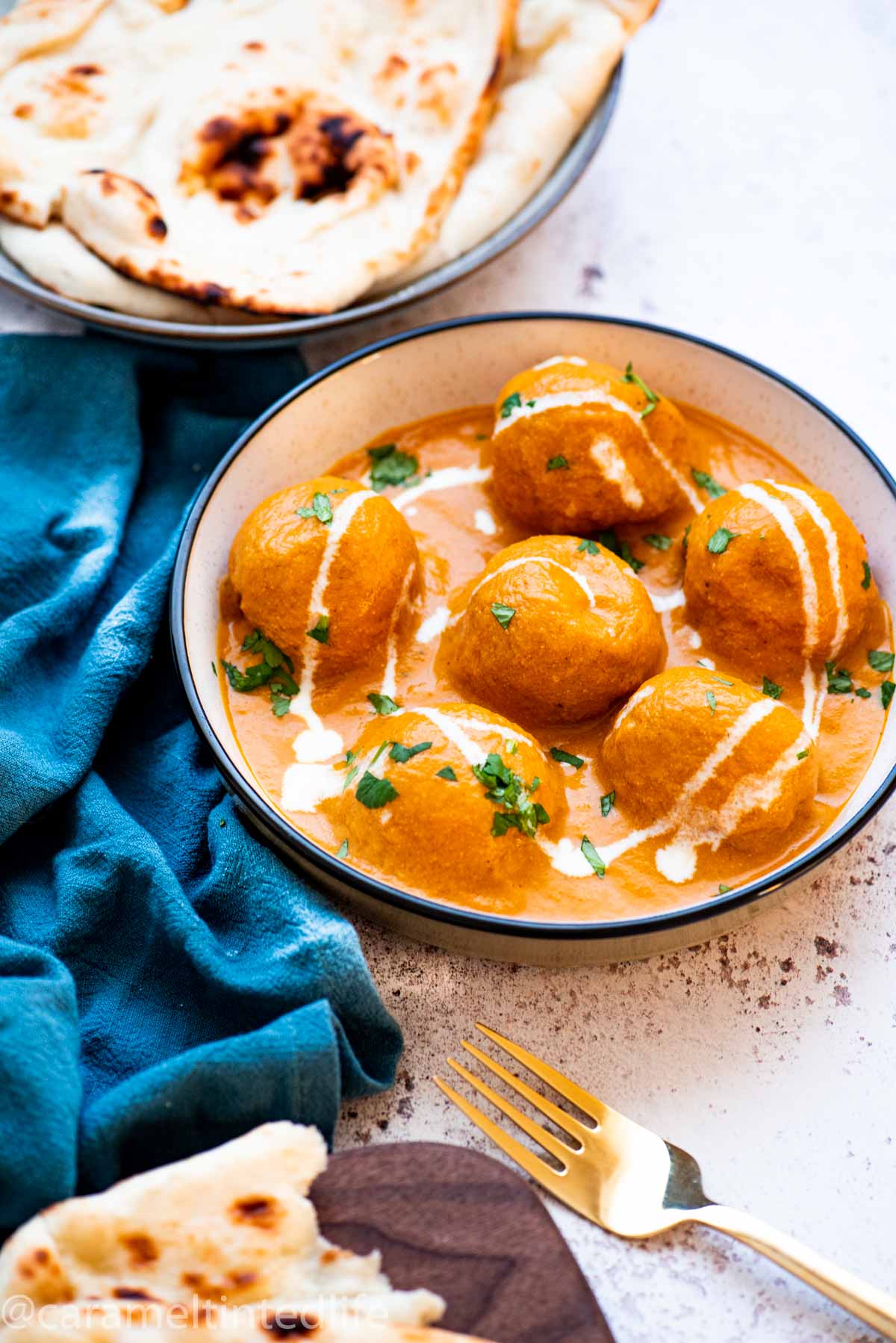Malai kofta in a bowl neyt to a bluw cloth and plates of naan