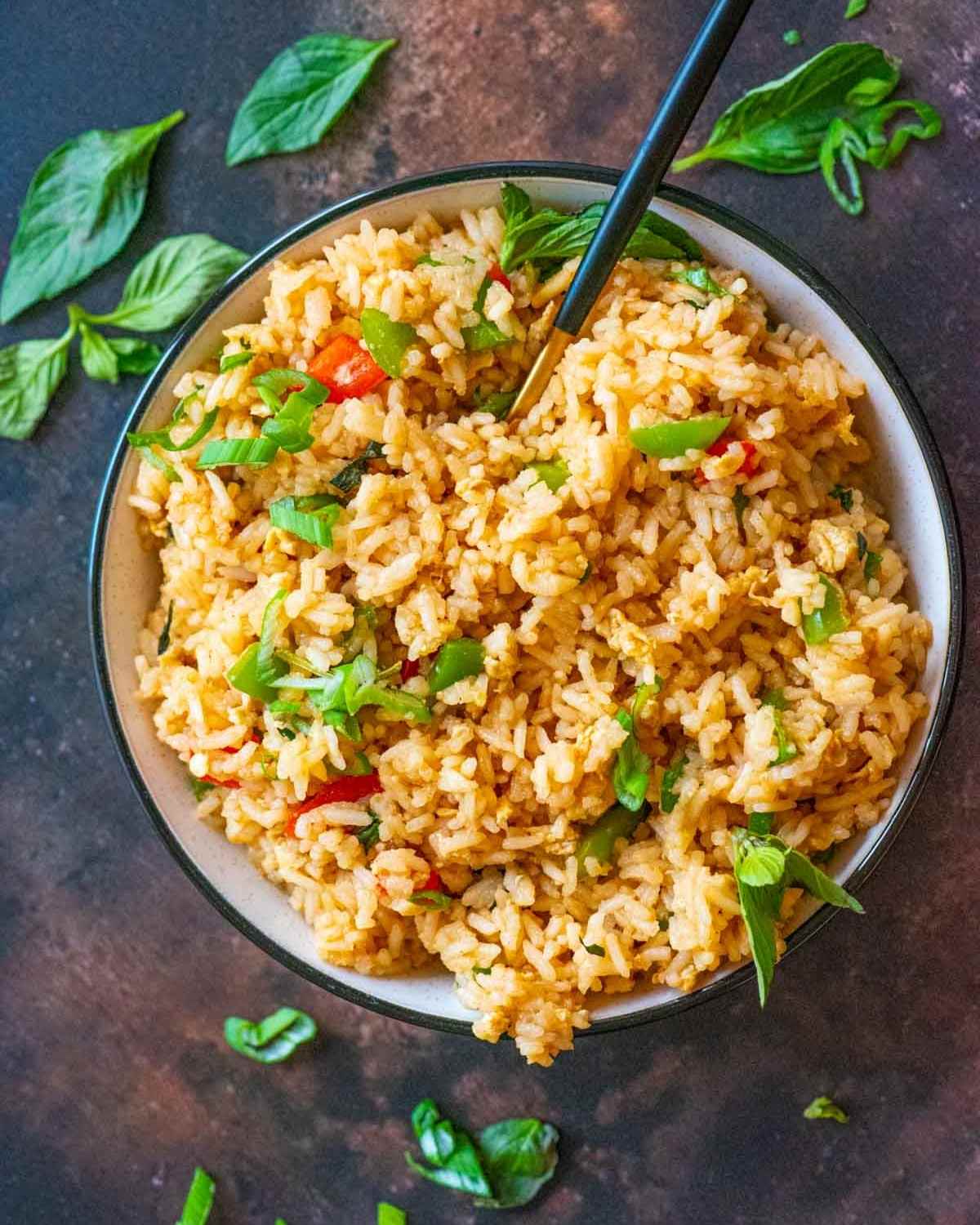 Top view of a bowl of fried rice and a serving spoon placed on a brown board