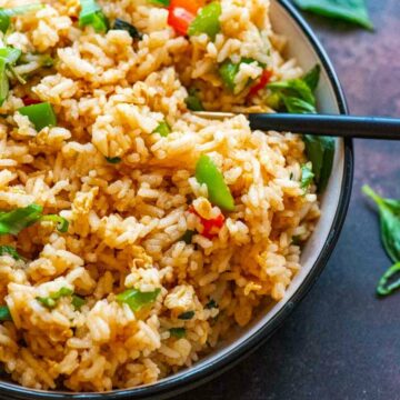 Closeup of a bowl of fried rice garnished with green onions and basil leaves scattered in the background