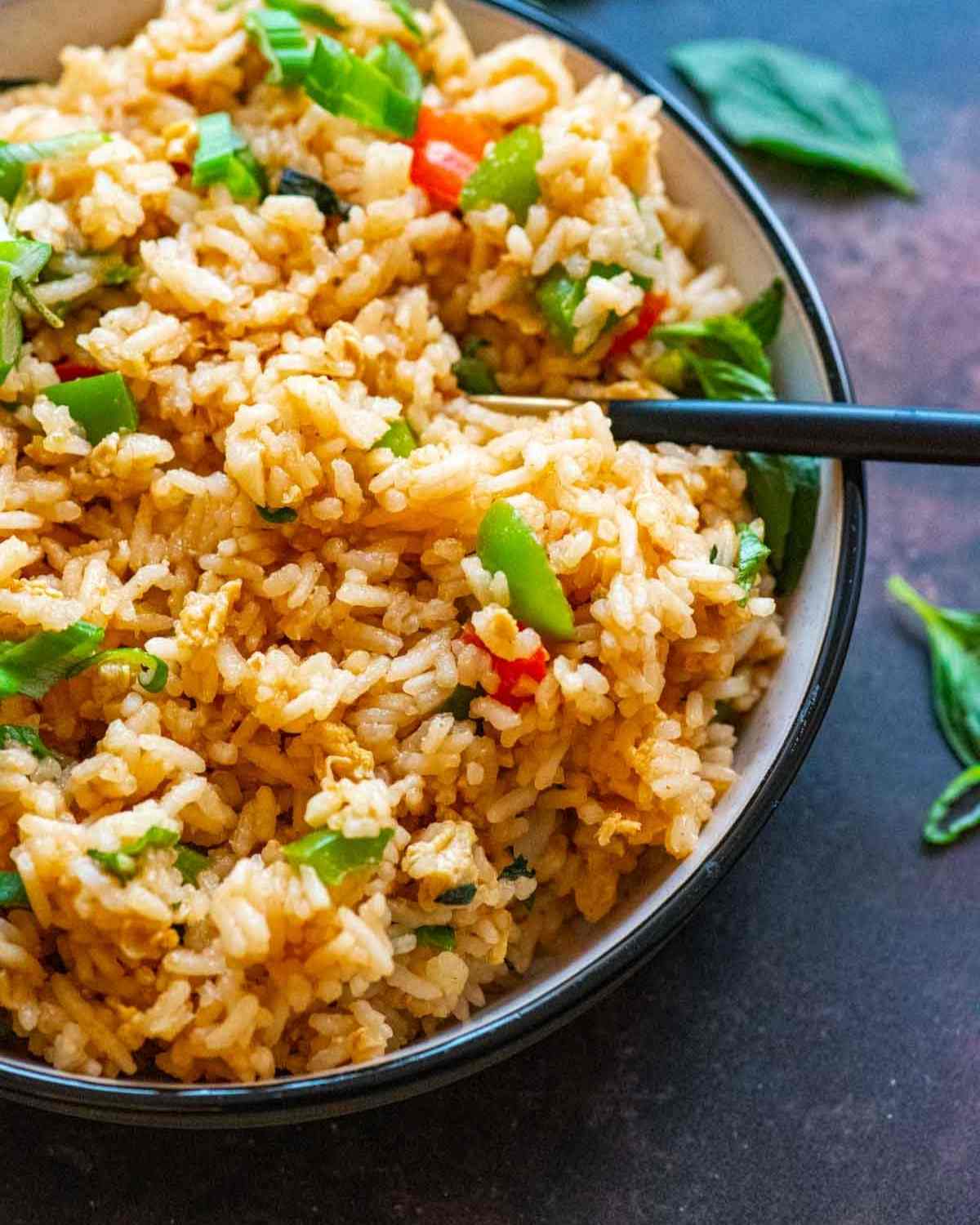 Closeup of a bowl of fried rice garnished with green onions and basil leaves scattered in the background