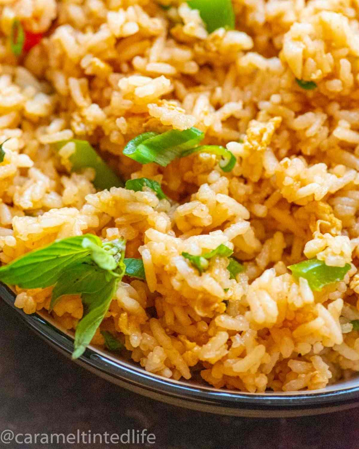 Closeup of fried rice in a bowl, garnished with a basil leaf cluster and green onions