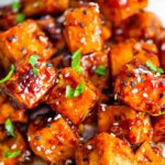 Crispy tofu coated in a sticky Asian sauce with sesame seeds and scallion garnish
