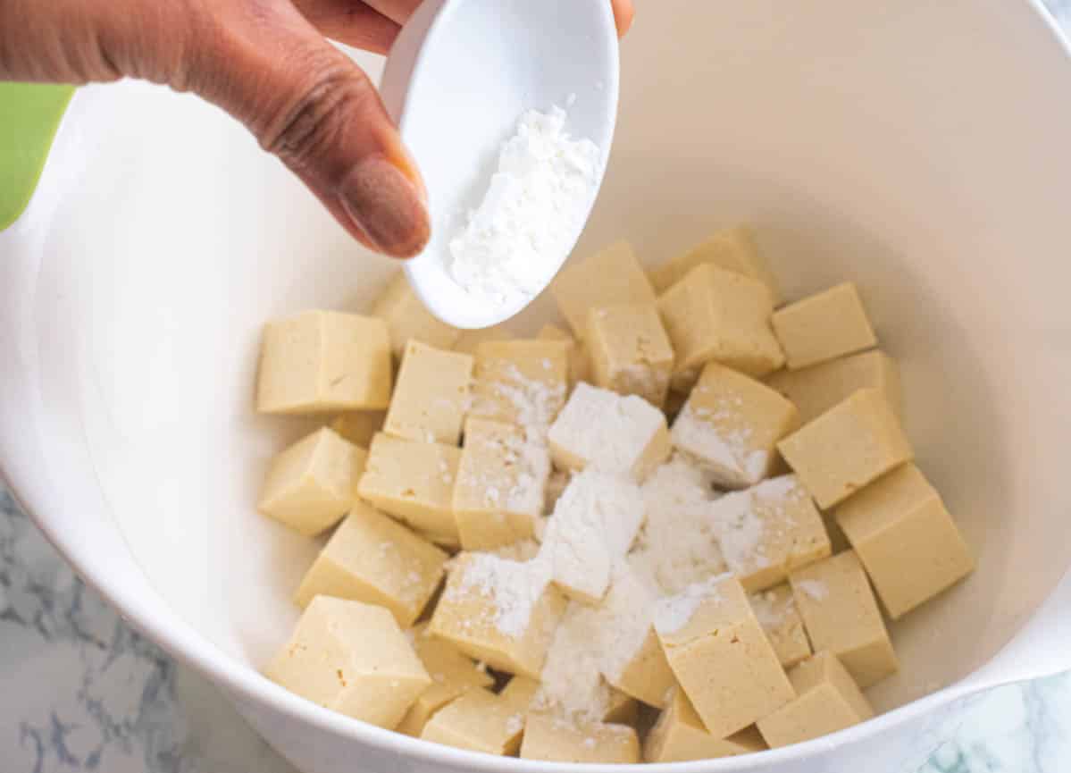 Adding corn starch in a bowl of tofu pieces in a mixing bowl