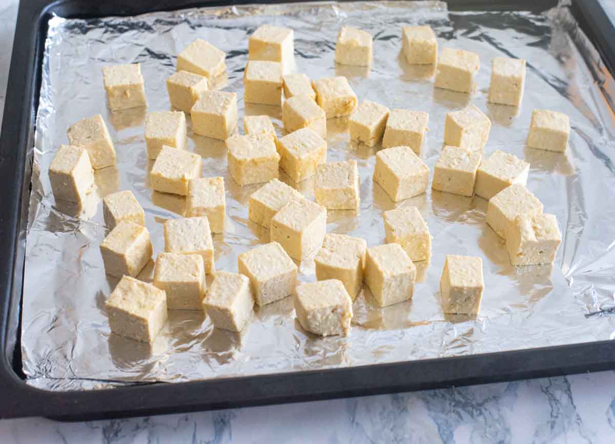 Tofu pieces spread out on a foil on a baking tray