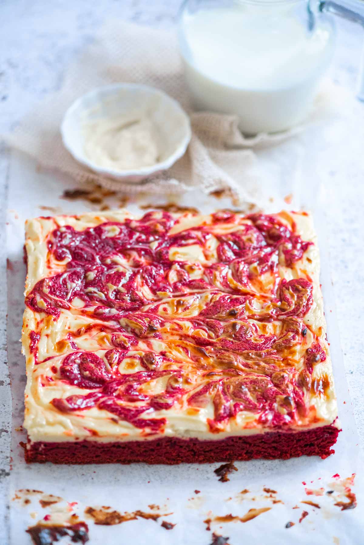 A square red velvet and cheesecake cake on a white board