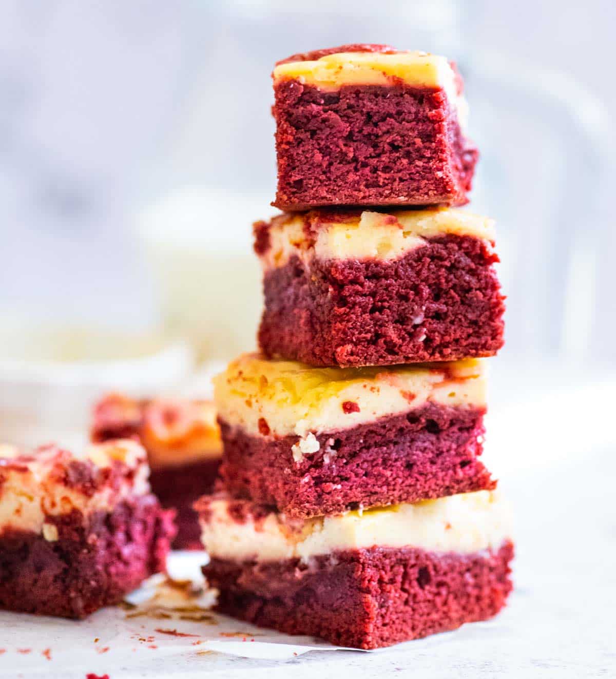 A stack of four red velvet and cheesecake brownies in the foreground, a milk jug in the background