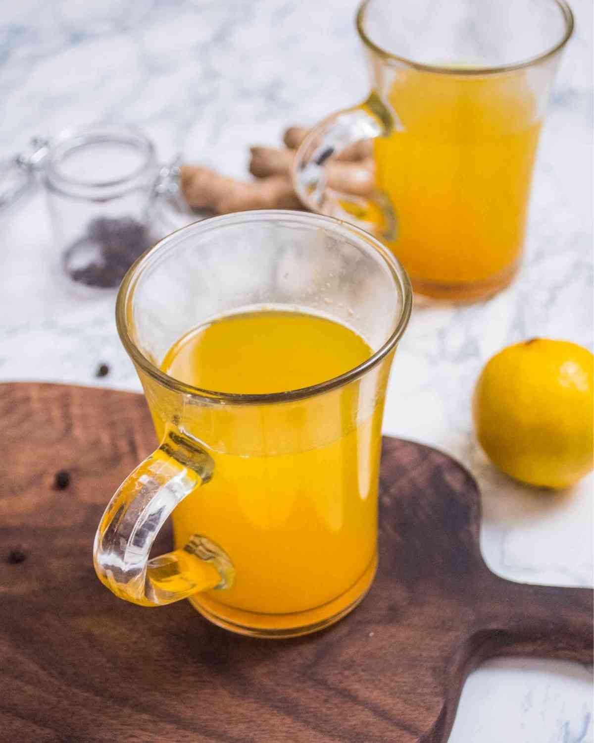 Two glasses of ginger and lemon drink served in glass mugs