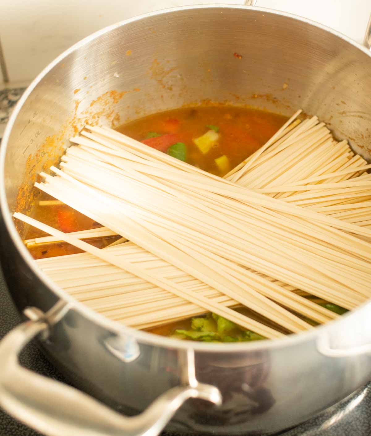 Raw udon noodles placed in a pot of soup on the stovetop