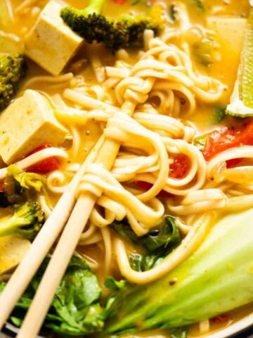 Close up of chopsticks holding noodles in a soup bowl