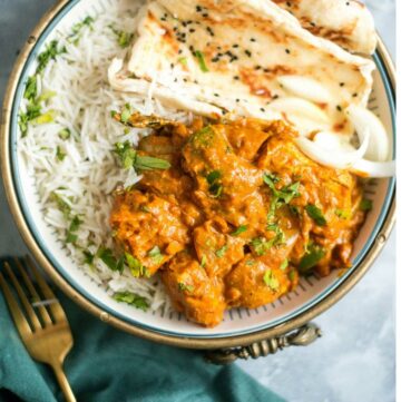 bowl of chicken in a thick sauce, with naan and rice