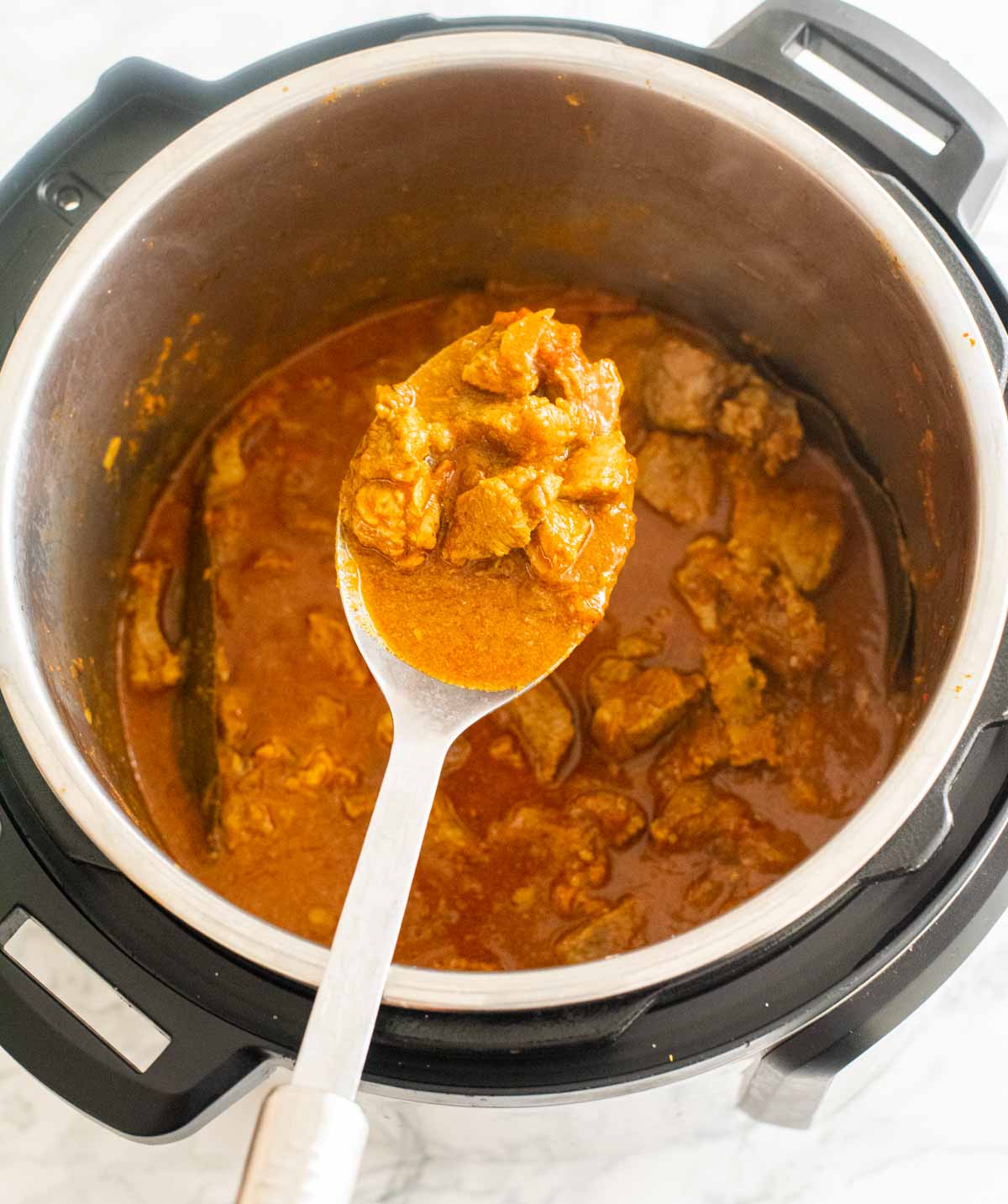 A ladle holding up lamb curry over an open Instant Pot 