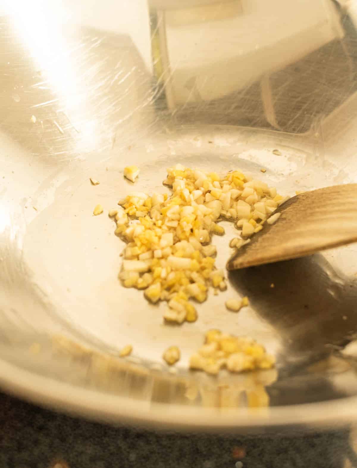Garlic being stir-fried in a wok with a wooden spatula