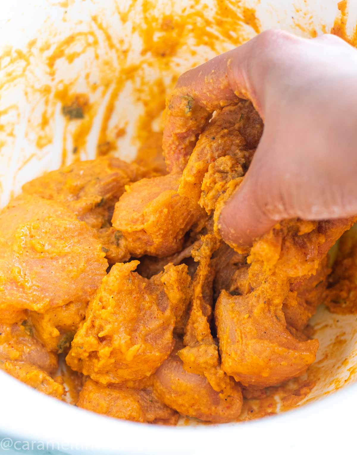 Hands mixing chicken pieces in a batter