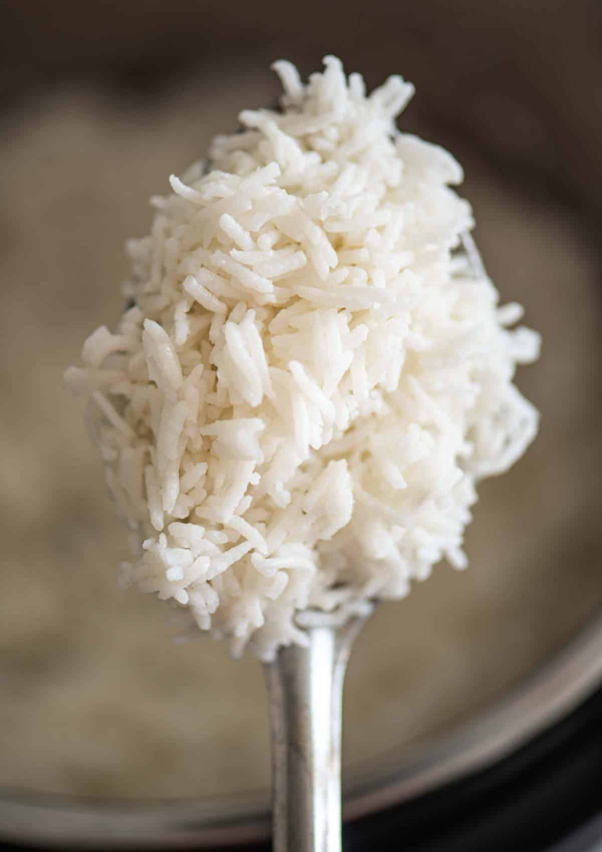 A spoon holding cooked basmati rice over an Instant Pot