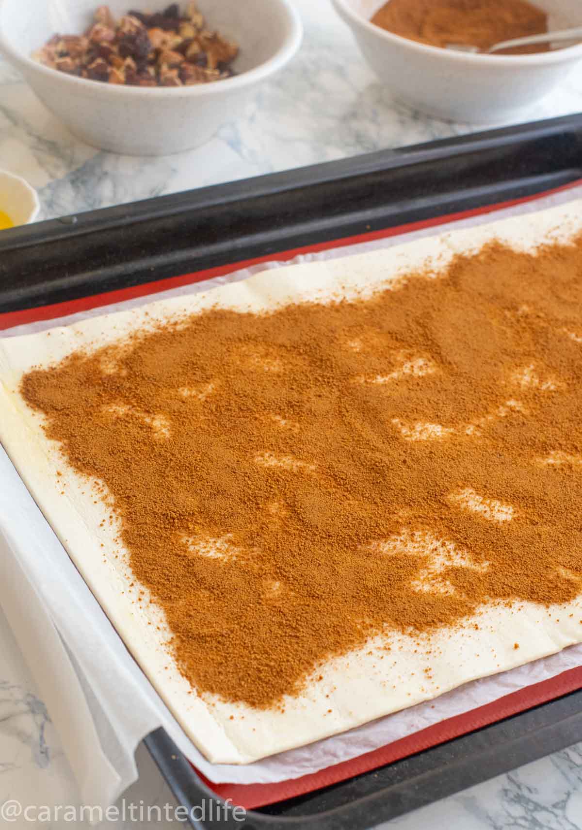 A sheet of puff pastry topped with cinnamon and brown sugar on a baking sheet 