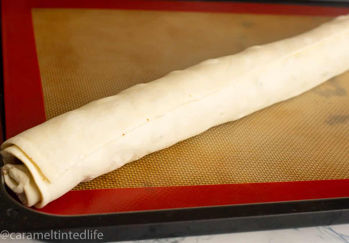A rolled up stuffed puff pastry sheet on a baking mat 