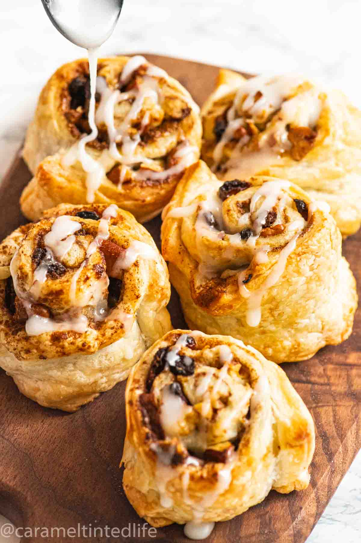 Icing being poured from a spoon on puff pastry rolls with cinnamon filling 