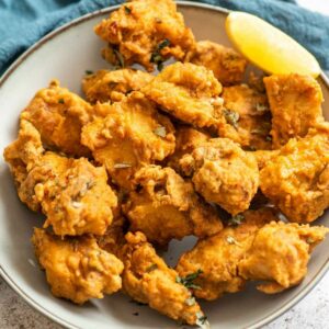 a bowl of chicken pakoras with lemon wedge