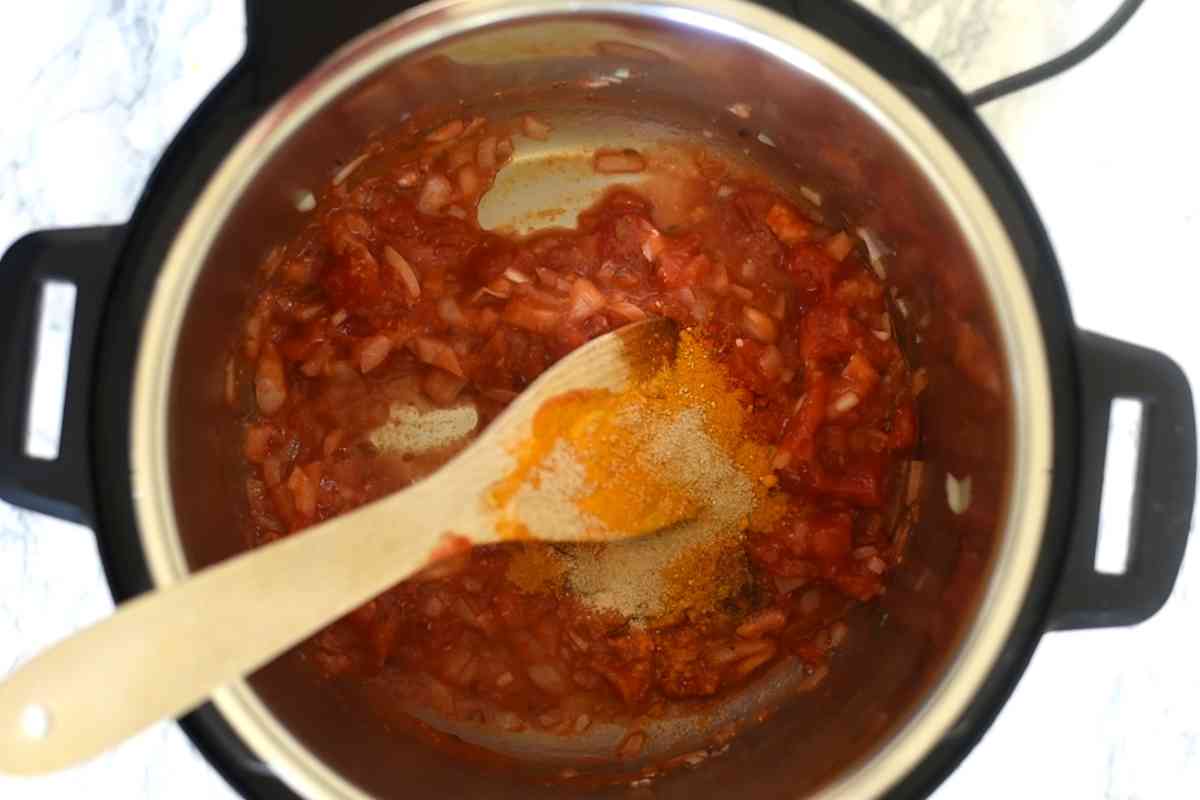 onions, tomatoes, spice powders with wooden spatula in an Instant Pot