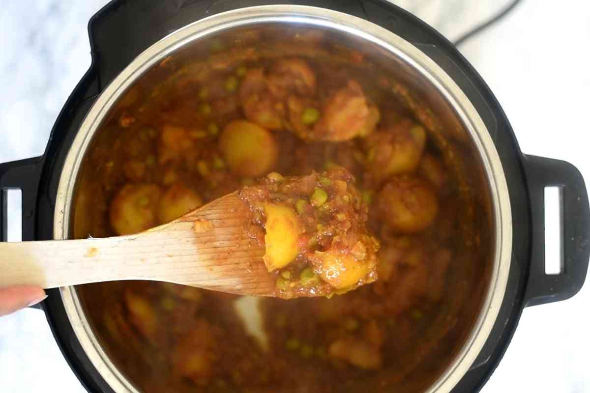 wooden spoon holding potatoes and peas curry above an Instant Pot