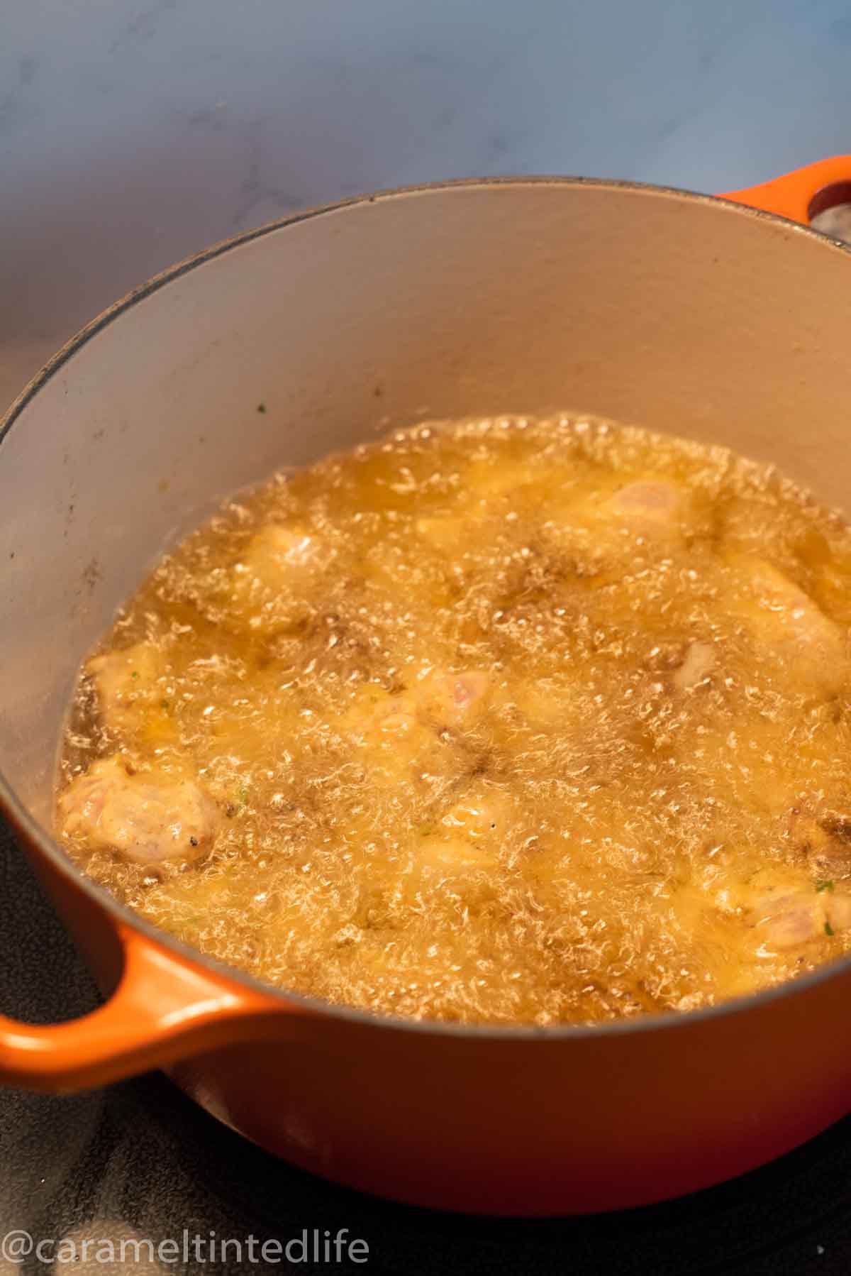 chicken pieces being deep fried in a cast iron pot