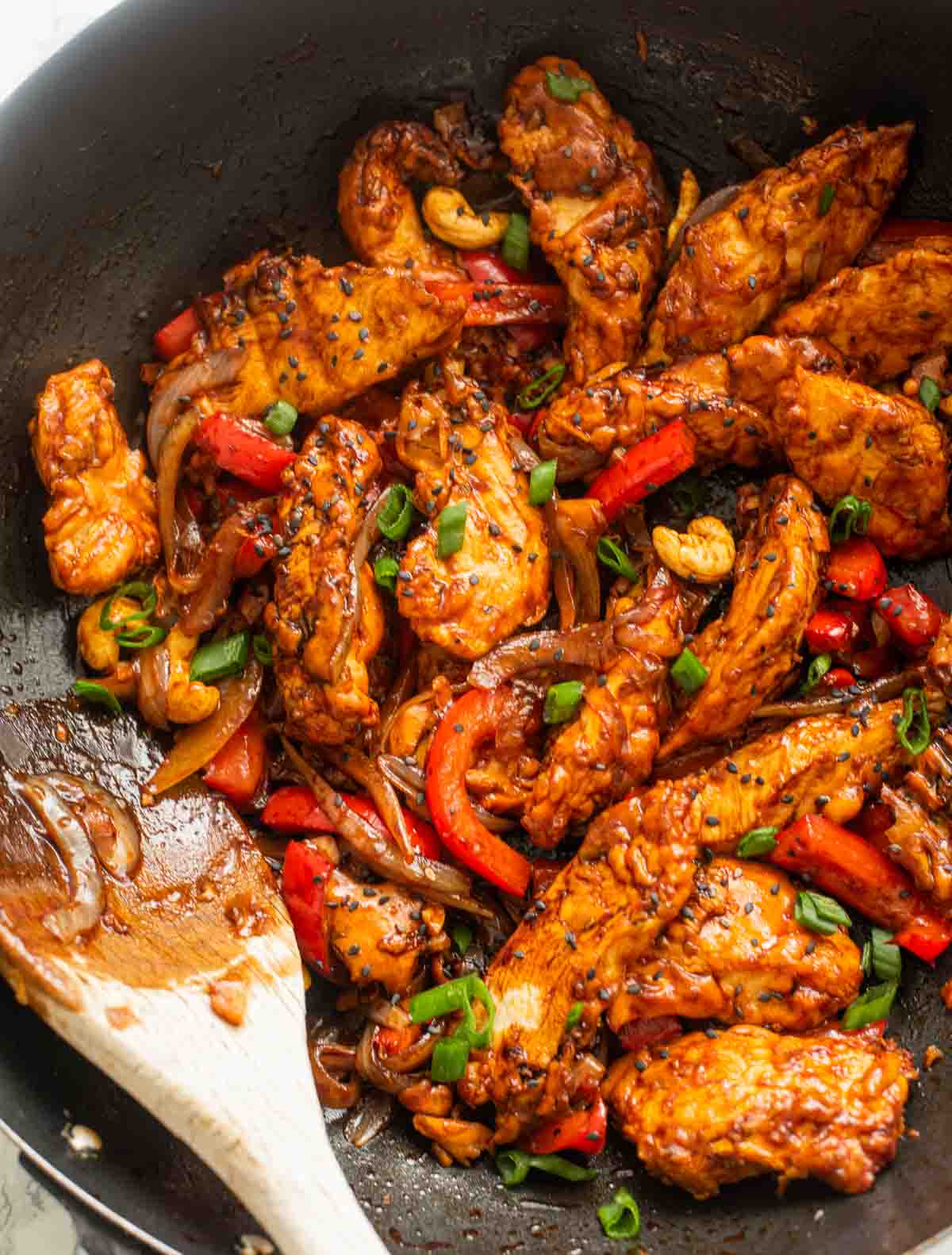 Chicken with bell peppers and scallions in a wok with wooden spatula