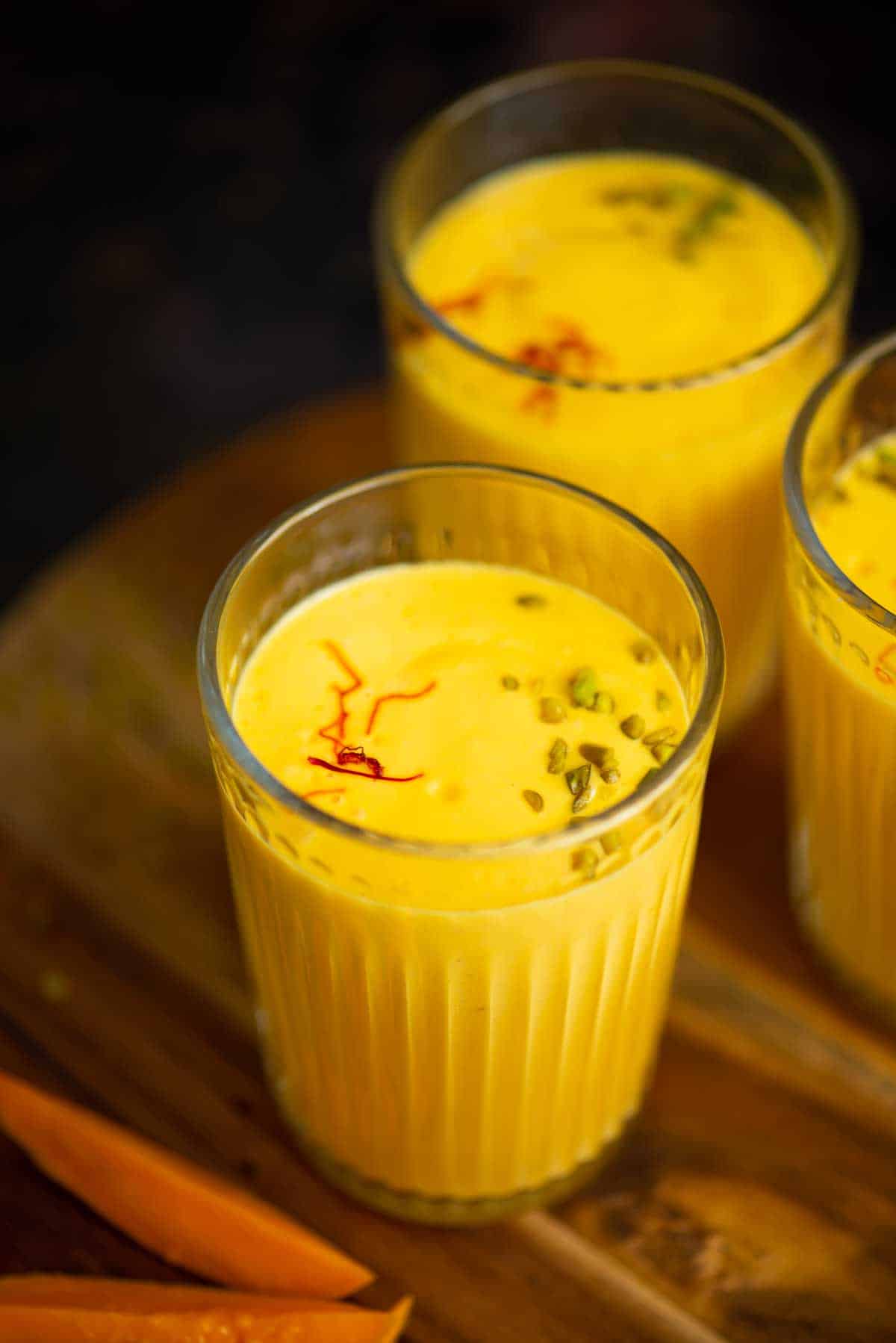 Close up of a glass of mango lassi garnished with saffron and pistachios