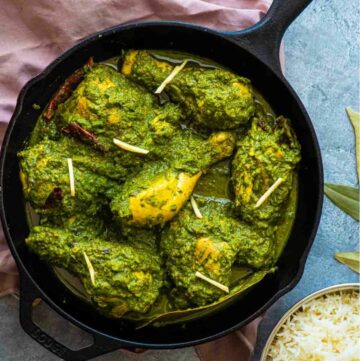 saag chicken in a cast iron pan on a blue background