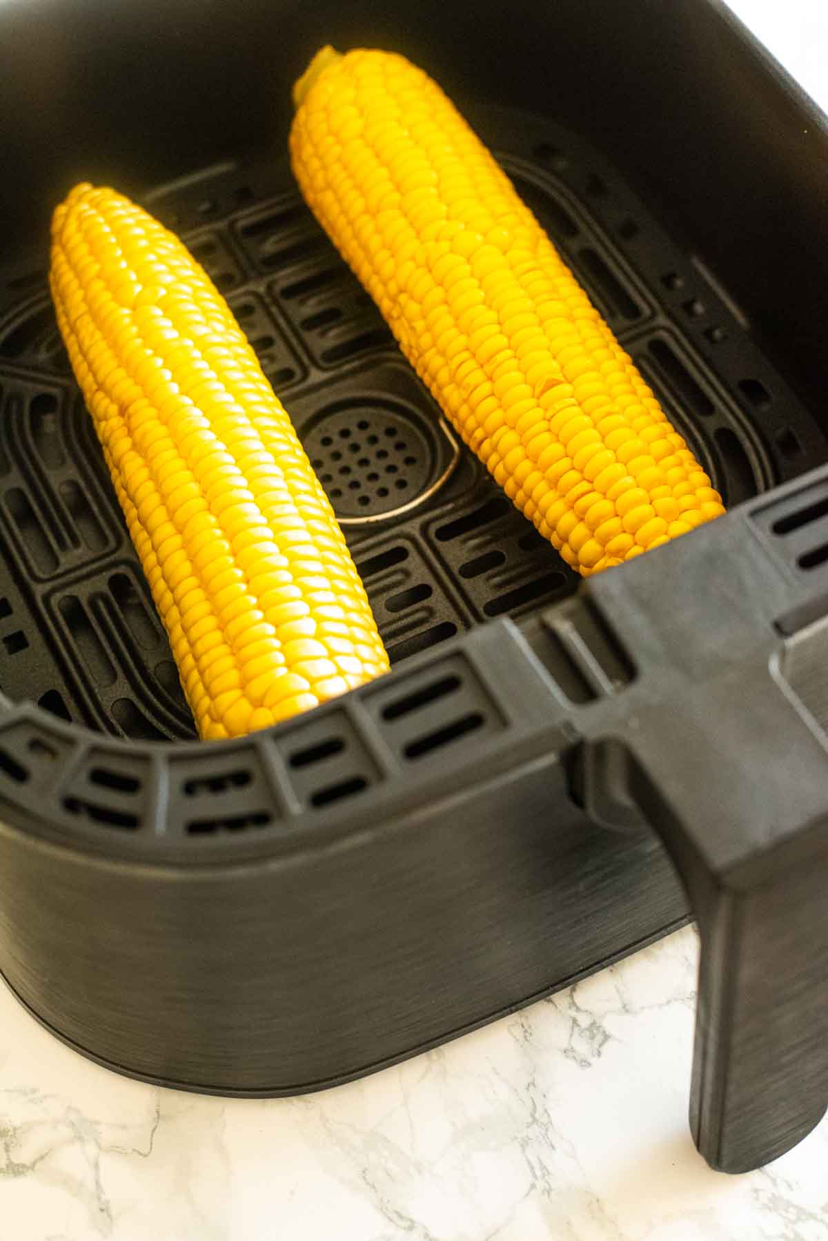 Two corn on the cobs in an air fryer