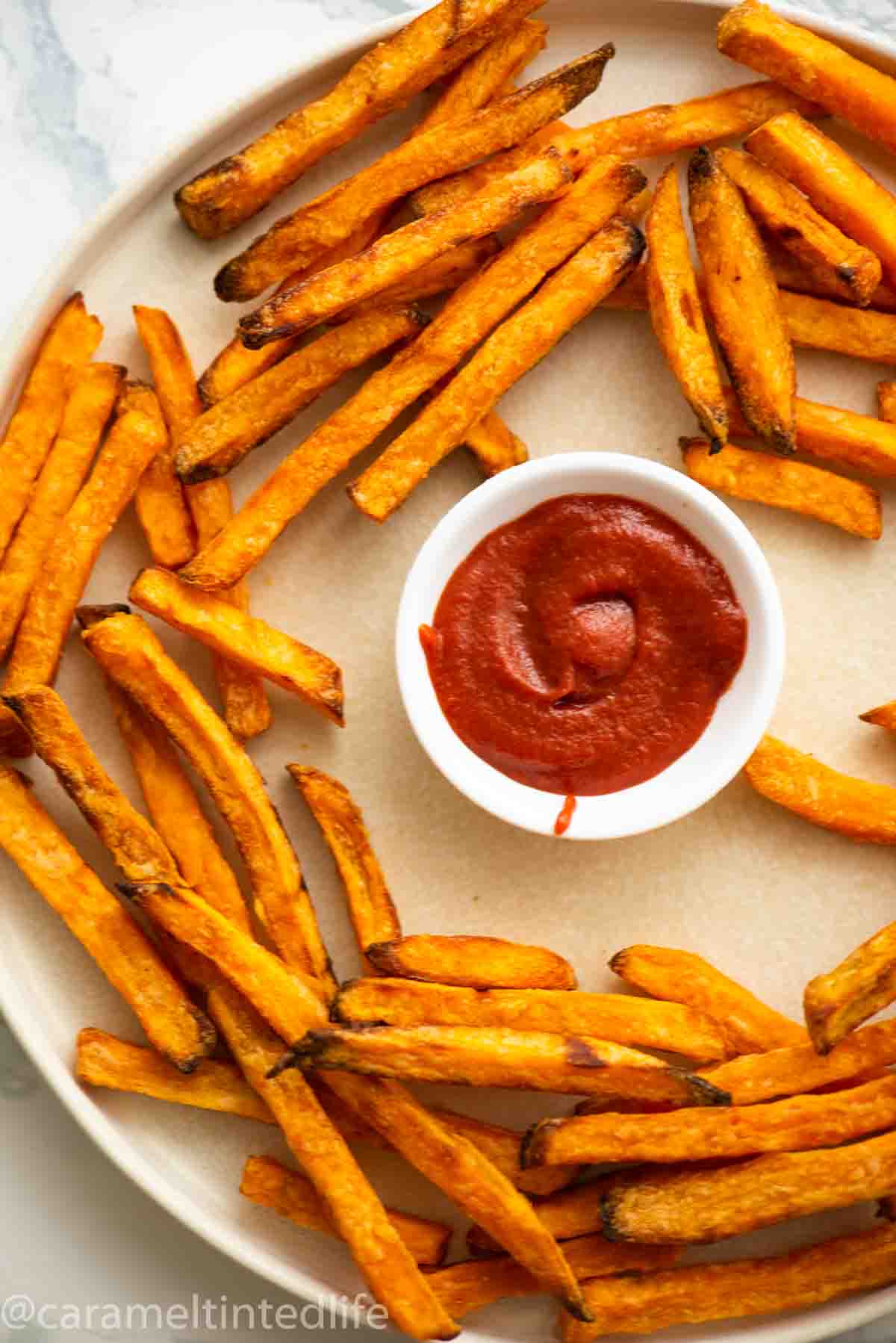 Sweet potato fries on a plate with ketchup in a bowl
